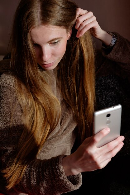 Rousse gingembre fille en capuche faisant selfie sur smartphone, assis sur le canapé et souriant