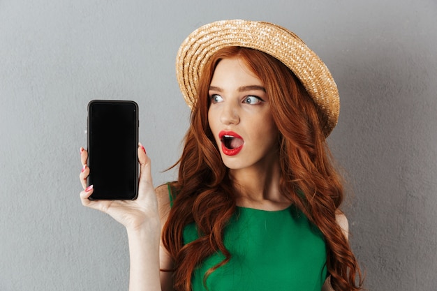 Rousse jeune femme choquée montrant l'écran du téléphone.