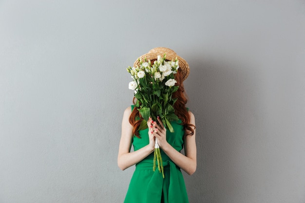 Rousse jeune femme couvrant le visage avec des fleurs.