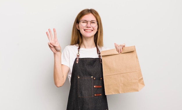 Rousse jolie fille souriante et amicale montrant le numéro trois employé à emporter