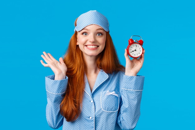 Rousse joyeuse et enthousiaste ne veut pas dormir trop longtemps, régler le réveil, tenir la montre rouge