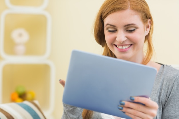 Rousse souriante assise sur le canapé avec tablette