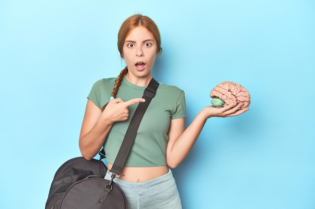 Rousse sportive avec un modèle de cerveau sur fond bleu pointant vers le côté