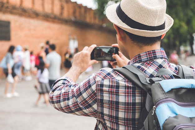 Routard mâle asiatique prenant des photos avec un smartphone à Tha Phae Gate, l'un des anciens monuments célèbres de la ville de Chiang Mai, Thaïlande