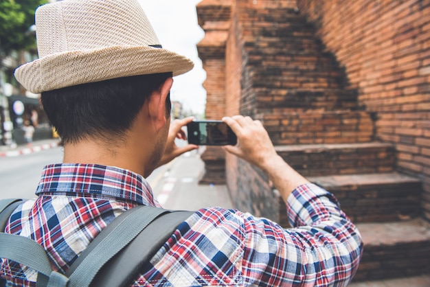 Routard mâle asiatique prenant des photos avec un smartphone à Tha Phae Gate, l'un des anciens monuments célèbres de la ville de Chiang Mai, Thaïlande