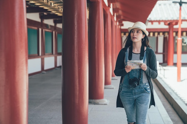 Routarde voyageuse regardant de côté tenant la carte sur le voyage de vacances d'été. Femme asiatique avec visite guidée livre histoire visite temple japonais shitennoji osaka japon. concept de personnes voyage tourisme