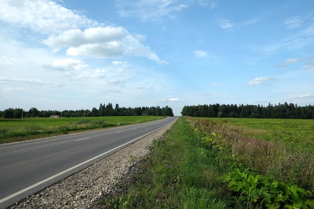 Photo route d'asphalte rurale vide avec des marquages routiers à travers les champs jusqu'à l'horizon