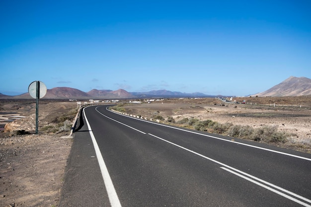 Route asphaltée avec un panneau d'avertissement sur fond de montagnes et de ciel bleu