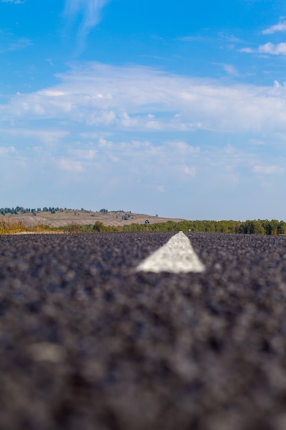 Route droite avec un marquage sur le fond de la nature. Route ouverte à l'avenir, pas de voitures, auto sur route goudronnée à travers la forêt verte, arbres. Nuages sur ciel bleu en été, soleil, journée ensoleillée. Vue de dessous