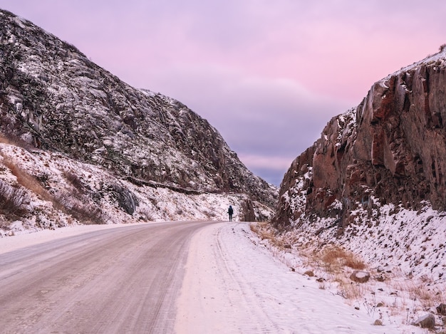 Une route enneigée qui s'étend au loin entre les collines. Péninsule de Kola. La couleur violette magique de l'aube.