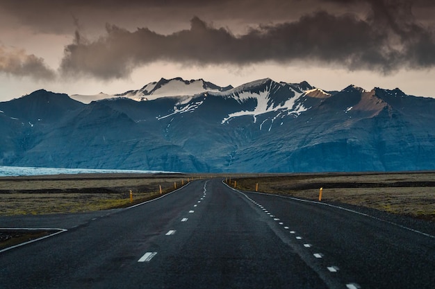 Route goudronnée droite avec tempête sur la montagne par une journée sombre en Islande