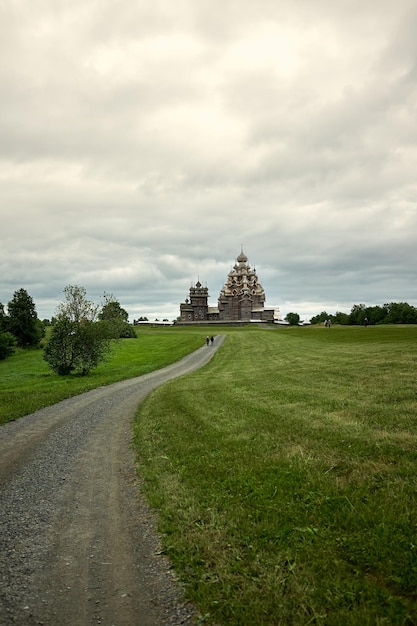 Une route de gravier mène à travers un champ jusqu'à une église orthodoxe en bois sur l'île de Kizhi Karelia