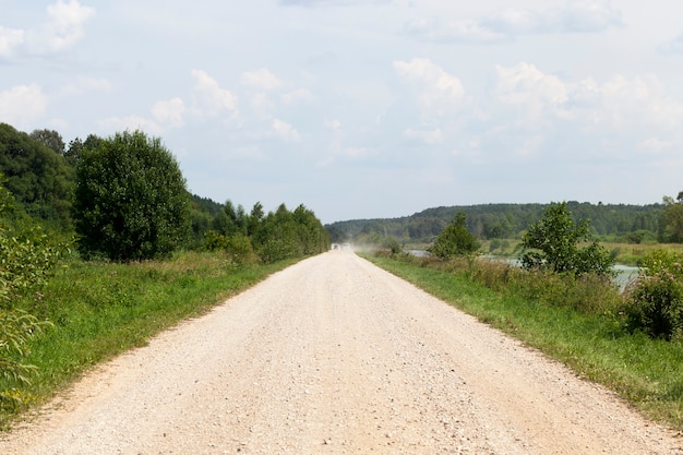 Route de gravier rurale, à l'horizon, la poussière des voitures qui passent, le paysage d'été