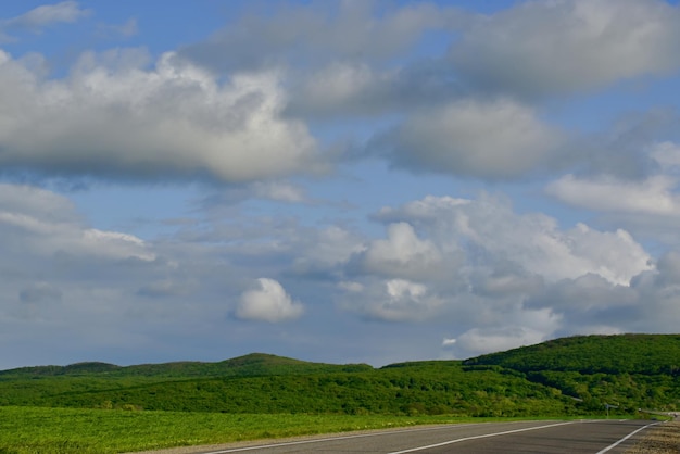 La route longe les collines verdoyantes sur fond de ciel bleu et de nuages moelleux Russie