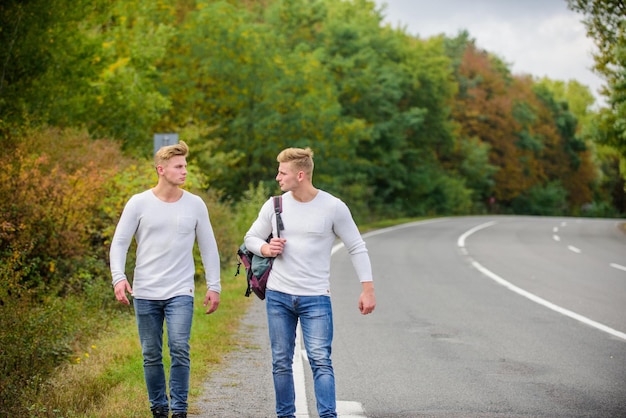 Route de marche de sac à dos d'hommes. Des jumeaux marchent le long de la route. Frères amis fond nature. Long chemin. Notion d'aventure. Les gars font de l'auto-stop sur la route. Arrêt automatique de voyage de voyageur de touriste. Problèmes de transport.