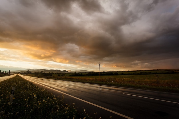 Route mouillée après la pluie et le coucher du soleil sur les champs