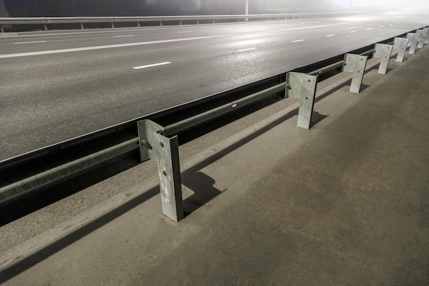 Route de nuit brumeuse vide illuminée avec garde-corps rigides