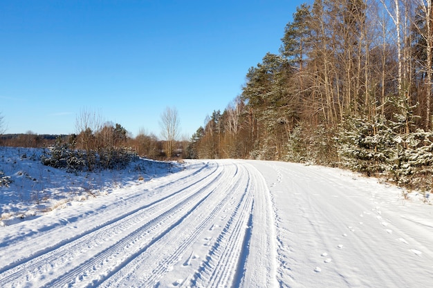 Route rurale couverte de neige pendant l'hiver. Sur les arbres au bord de la route. Sur la neige, les empreintes digitales visibles des pneus de voiture et de la faune slezhdy. Gros plan photographié.