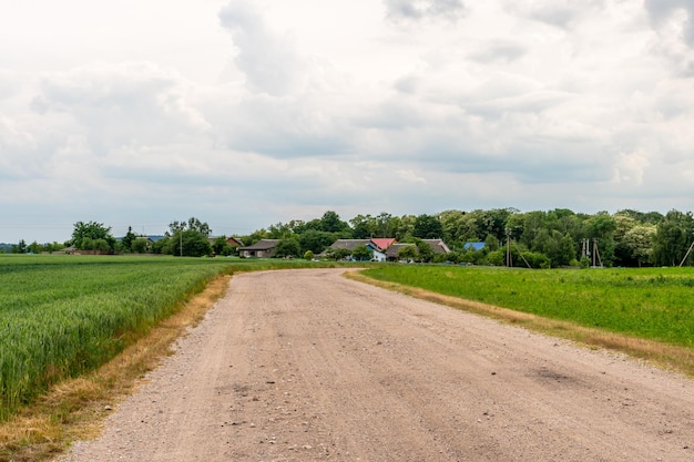 Une route sablonneuse sèche traverse un champ sous le soleil brûlant et les nuages Route de terre à l'extérieur de la ville dans le village Climat aride sur terre Le changement climatique et ses conséquences