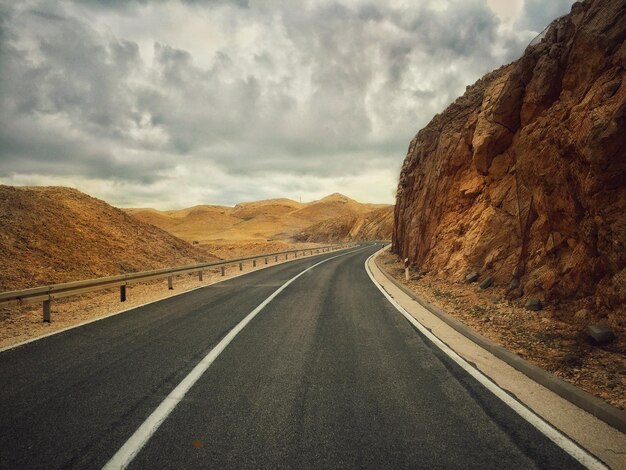 Une route vide contre un ciel nuageux