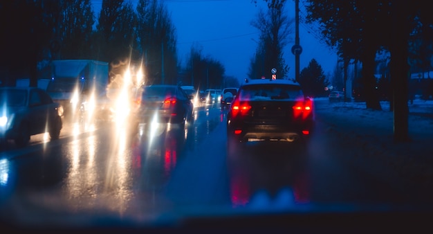 Route de la ville de nuit à travers les voitures pare-brise fond abstrait goutte d'eau sur les lumières en verre et la pluie.