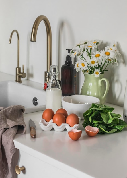 La routine du matin prépare le petit-déjeuner Oeufs lait épinards sur une table de cuisine blanche ingrédients d'omelette