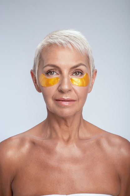 Routine matinale. Joyeuse femme âgée gardant le sourire sur son visage et utilisant des cache-œil