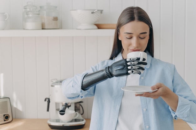 Routine d'une personne handicapée Une jolie fille handicapée tient une tasse de thé avec une main cybernétique