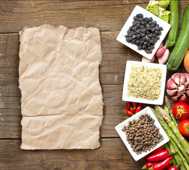 Roveja, graines de chanvre et pois chiches noirs dans des bols et des légumes sur une vue de dessus de table en bois avec copie papier