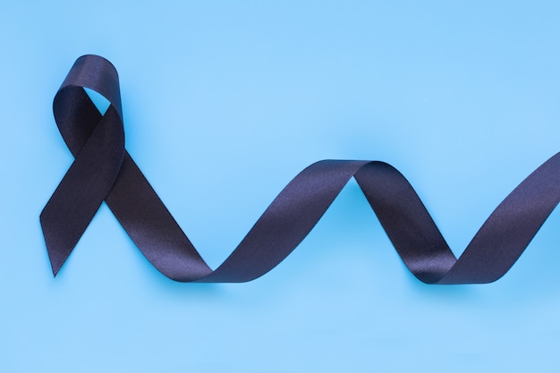 Ruban noir curl sur fond isolé bleu avec espace copie, symbole du concept de sensibilisation au cancer de la peau.