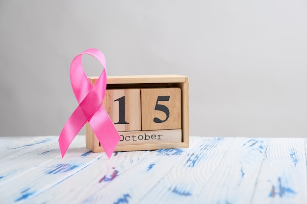 Ruban rose et calendrier de cube en bois fixés pour le 15 octobre sur une table en bois.