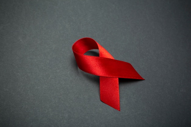 Photo ruban rouge sur fond gris foncé. symbole de la journée mondiale du sida ou du mois de la sensibilisation au cancer ou au vih et concept de soins de santé. espace copie