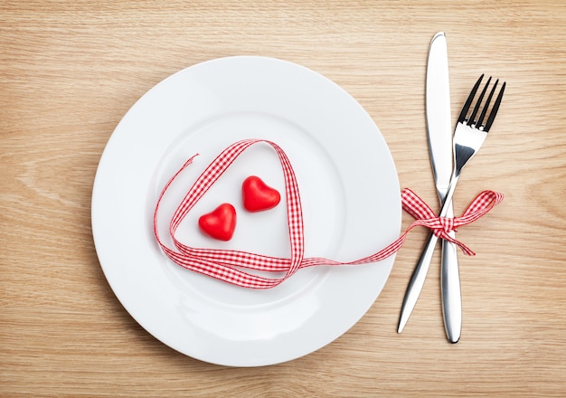 Ruban rouge en forme de coeur de la Saint-Valentin sur une assiette avec de l'argenterie. Sur fond de table en bois