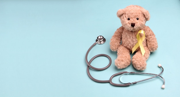 Ruban Teddy Bear en or jaune avec stéthoscope sur fond bleu.