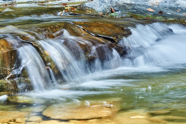 Un ruisseau clair coule sur les pierres, formant une petite cascade, les jets d'eau sont flous en mouvement