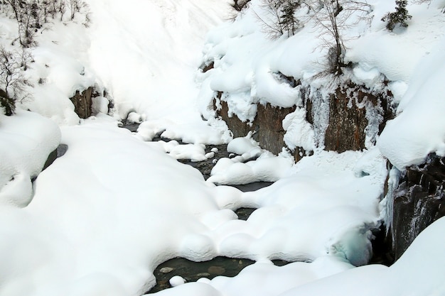 Le ruisseau de montagne coule parmi les rochers et la neige blanche gonflée sur les rives