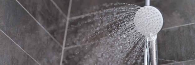 Des ruissellements d'eau s'écoulant de la pomme de douche dans la salle de bain en gros plan