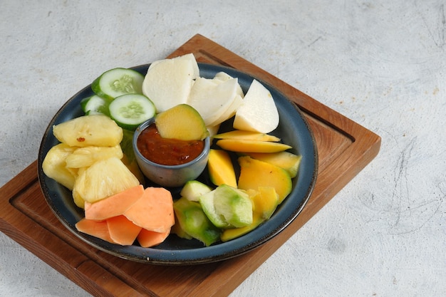 rujak buah ou salade de fruits indonésienne sur assiette blanche servie avec sauce épicée douce et arachide moulue