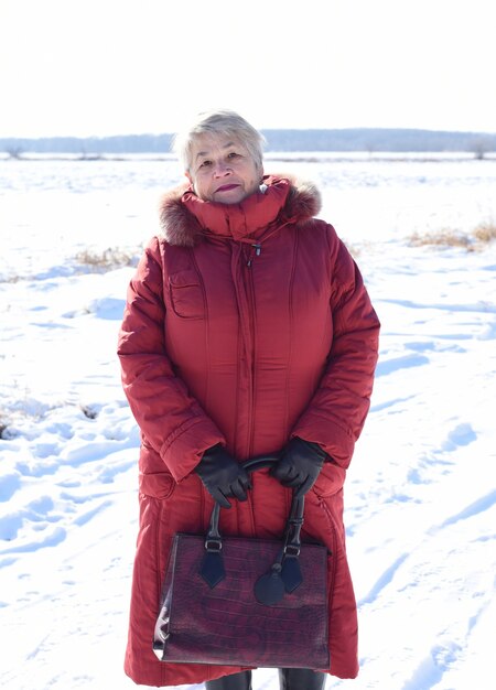 Russe 67 ans senior woman in red coat regardant la caméra contre champ neigeux