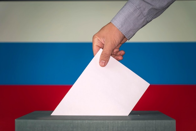 La russie le symbole des élections La main masculine pose une feuille de papier blanche avec une marque comme symbole d'un bulletin de vote sur le fond du drapeau de la russie