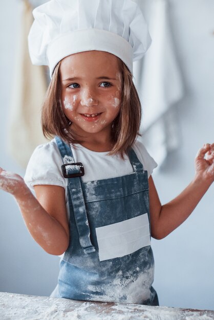 S'amuser. Enfant mignon en uniforme de chef blanc préparant la nourriture dans la cuisine.