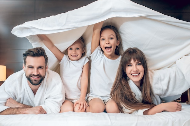 S'amuser. Enfants et parents souriants en position couchée sous la couverture