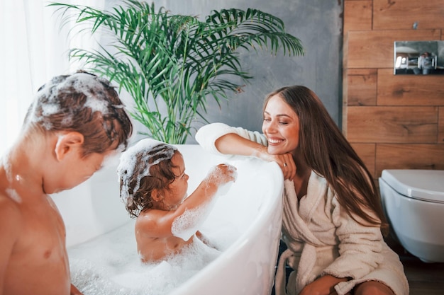 S'amuser Une jeune mère aide son fils et sa fille Deux enfants se lavent dans le bain