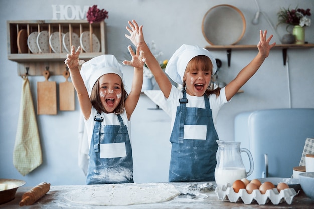 S'amuser pendant le processus. Enfants de la famille en uniforme de chef blanc préparant la nourriture dans la cuisine.