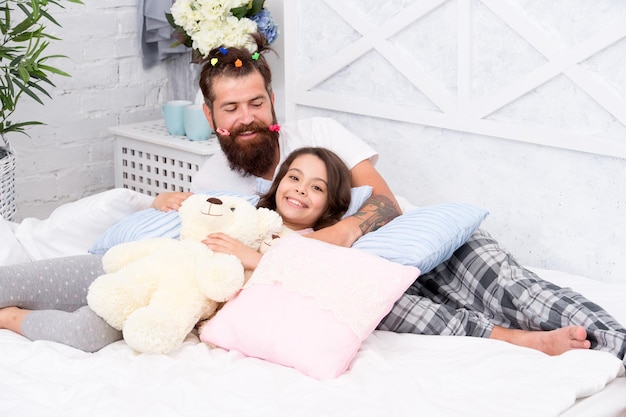 S'amuser en pyjama Soirée pyjama Paternité heureuse Amis proches Papa et fille se détendant dans la chambre Style pyjama Père homme barbu avec des queues de cheval drôles de coiffure et fille en pyjama