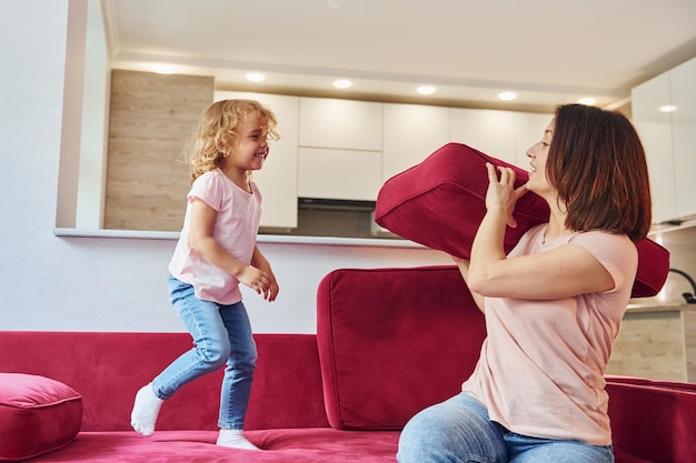 S'amuser et sauter Jeune mère avec sa petite fille dans des vêtements décontractés ensemble à l'intérieur à la maison