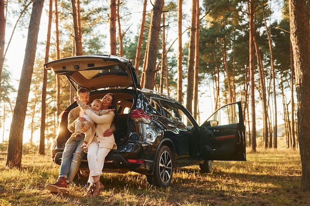 S'appuyant sur la voiture Famille heureuse de père mère et petite fille est dans la forêt