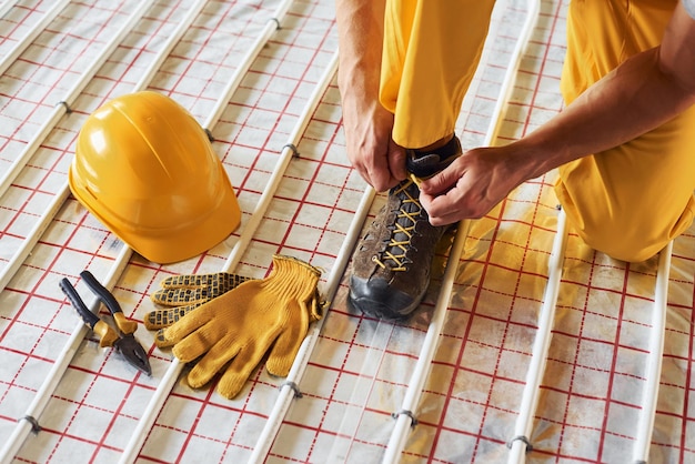 S'assoit et porte des chaussures Travailleur en uniforme de couleur jaune installant un système de chauffage par le sol