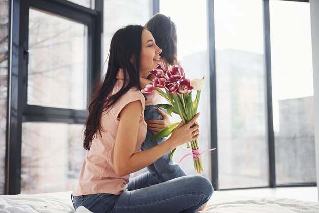 S'embrasser La fille félicite la mère avec les vacances et donne un bouquet de fleurs