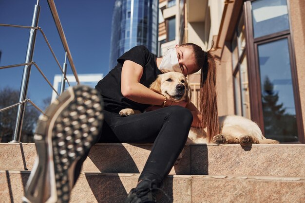 S'embrasser Jeune femme positive portant un masque de protection assise avec son chien au moment du coronavirus de quarantaine